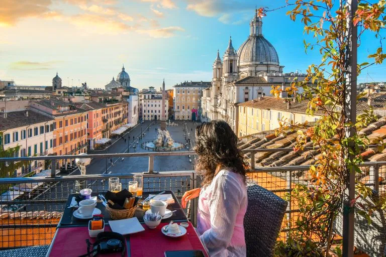 Een vrouw geniet van het uitzicht op Rome, Italië en het Piazza Navona terwijl ze haar continentale ontbijt afmaakt vanaf een dakterras van een luxe hotel op een vroege zomerochtend.