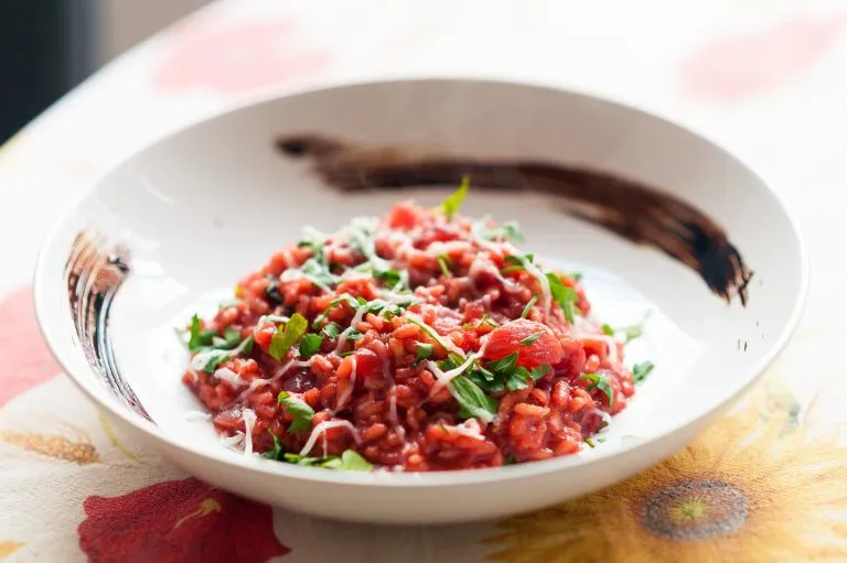 Nahaufnahme eines italienischen roten Gourmet-Risottos mit Rüben, Petersilie, Käse und Balsamico-Essig aus Modena in einem weißen Teller auf einem Tisch mit Tuch